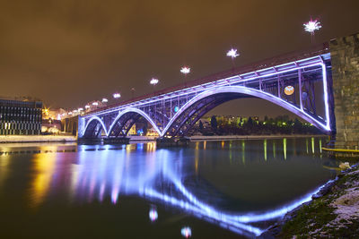 Illuminated bridge over river against sky at night