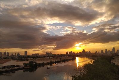 Scenic view of river by buildings against sky during sunset