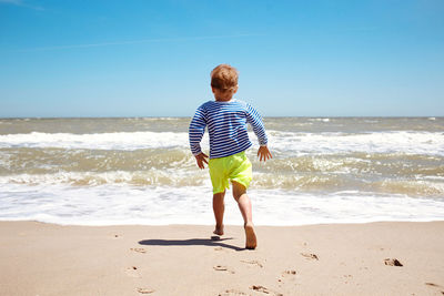 Little boy run barefoot to the sea, happy summer childhood