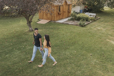 Smiling couple holding hands while walking at backyard