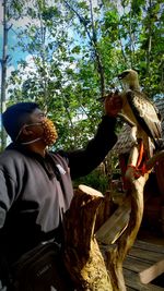 Man holding bird on plant against trees