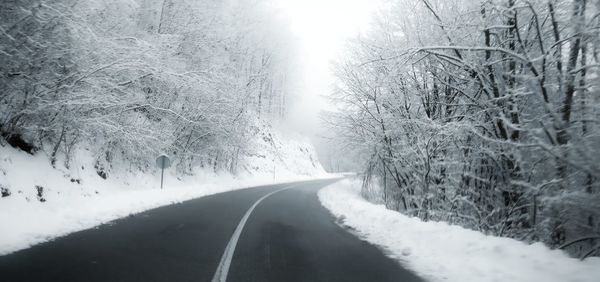 Snow covered road amidst trees against sky