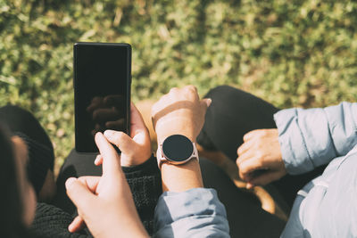 Hispanic  teenager holding smartphone looking while sitting on grass with hispanic mother and sister