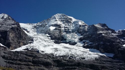 Low angle view of snowcapped mountains against clear blue sky