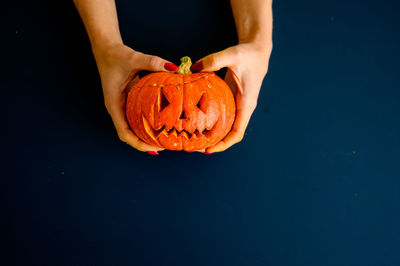 Person hand holding pumpkin against blue background