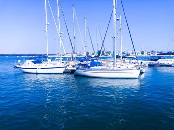 Sailboats moored in sea against clear blue sky