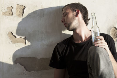 Young man drinking glass against wall