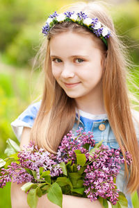 Smiling blonde teen girl 14-15 year old holding flowers over nature green background close up.