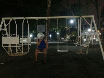 Rear view of boy sitting at illuminated street lights at night