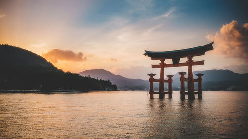 Torii gate in lake against sky during sunset