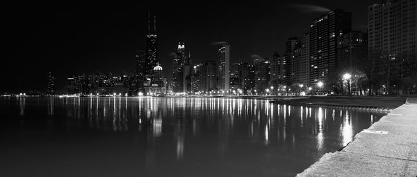 Illuminated buildings by river against sky at night