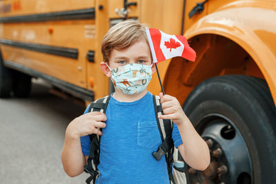 Portrait of boy holding camera while standing by car