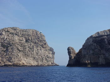 Rock formations by sea against blue sky