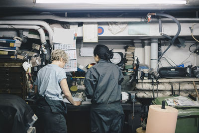 Rear view of female coworkers standing by workbench at auto repair shop