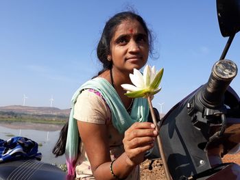 Portrait of woman holding flower against sky