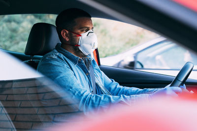Man with mask and gloves driving a car.
