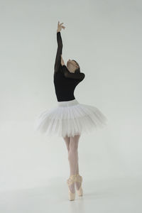 A ballerina in a bodysuit and tutu poses in motion showing ballet elements while standing on pointes