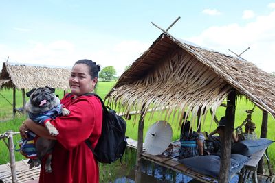 Portrait of mid adult woman carrying pug while standing against sky at farm