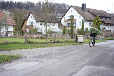 Rear view of man riding bicycle on road by buildings