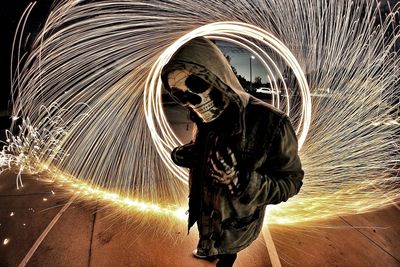 Man wearing spooky mask standing by wire wool at night