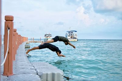 Men jumping in sea against sky