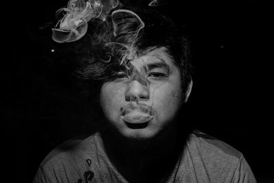 Close-up portrait of young man smoking against black background