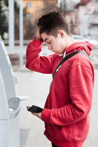 Side view of young man standing by atm machine