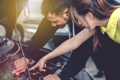 Woman pointing on engine while man repairing car