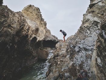 Woman standing on rock formation at sea against sky