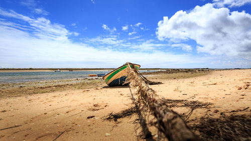 Fishing boat moored at beach against cloudy sky