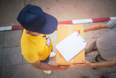 High angle view of delivery man giving parcel to customer by building in city