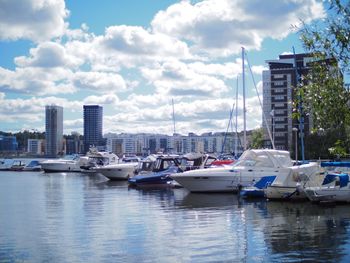 Boats moored at harbor against sky in city