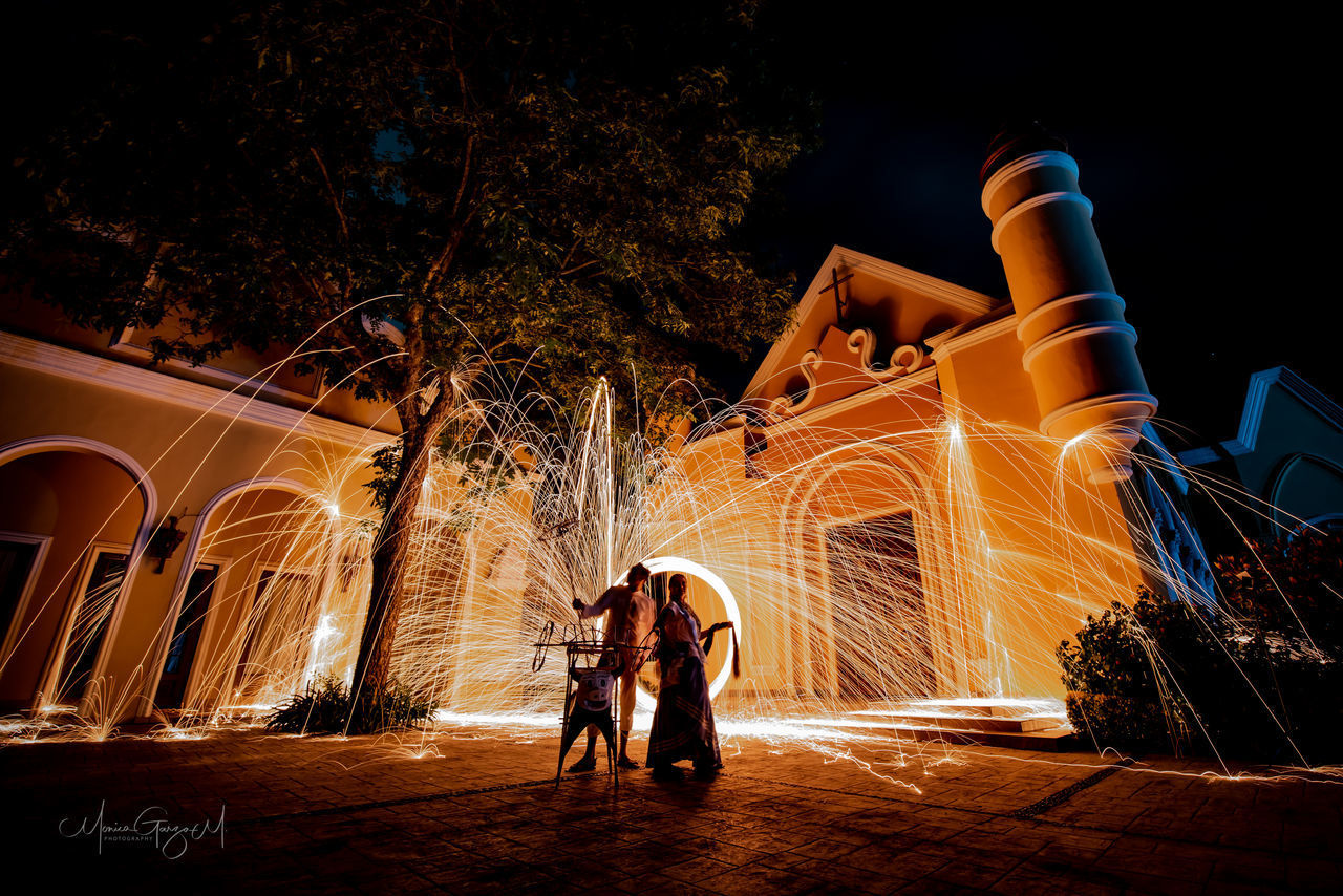 PEOPLE STANDING AGAINST ILLUMINATED BUILDINGS