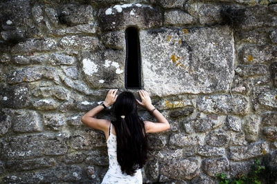 Girl trying to see through a little window in a stone wall