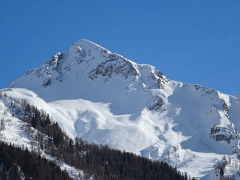 Low angle view of snowcapped mountains against clear blue sky