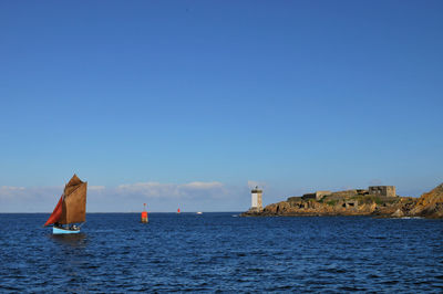 Sailboat on sea against clear blue sky