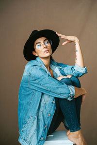 Portrait of young woman wearing hat against wall