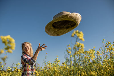 Portrait of a girl throwing a straw hat in a rapeseed field