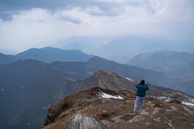 Rear view of man standing on mountain against sky