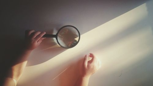 Cropped hands of child holding magnifying glass against wall