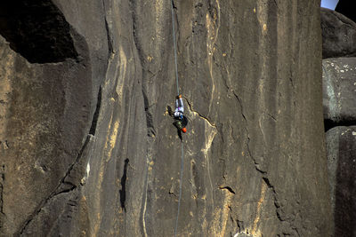 Low angle view of upside down man hanging from rope against cliff