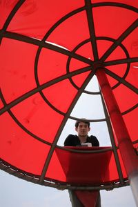 Low angle portrait of teenage boy standing by parasol