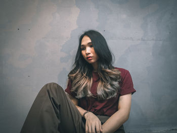 Beautiful young woman sitting against wall