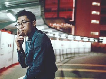 Side view of young man looking away while smoking cigarette in city at night