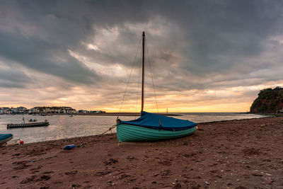 Sailboats moored on beach against sky during sunset