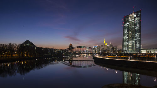 Illuminated bridge over river by buildings against sky at night