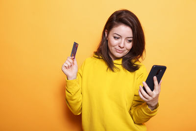 Young woman using mobile phone against yellow background