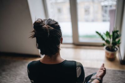 Rear view of woman doing yoga while sitting at home