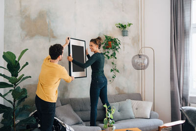 Mid adult man passing picture frame to girlfriend against wall at new home