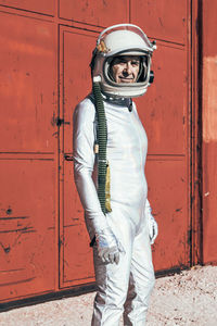 Man in spacesuit standing near red wall of industrial facility on sunny day